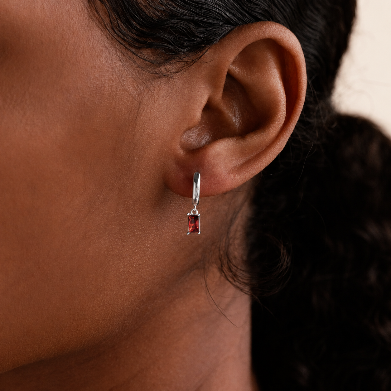 Close-up of an ear wearing a silver earring with a red gemstone.